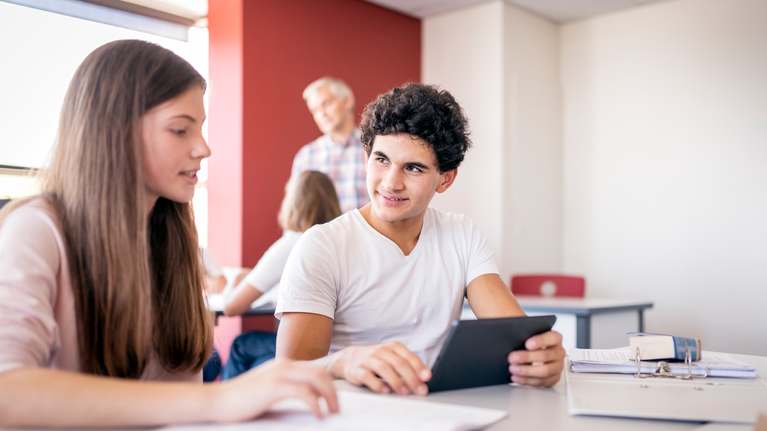 Male and female teenager student in classroom using technology