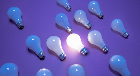 Lightbulbs on a purple background. One lightbulb is lit.